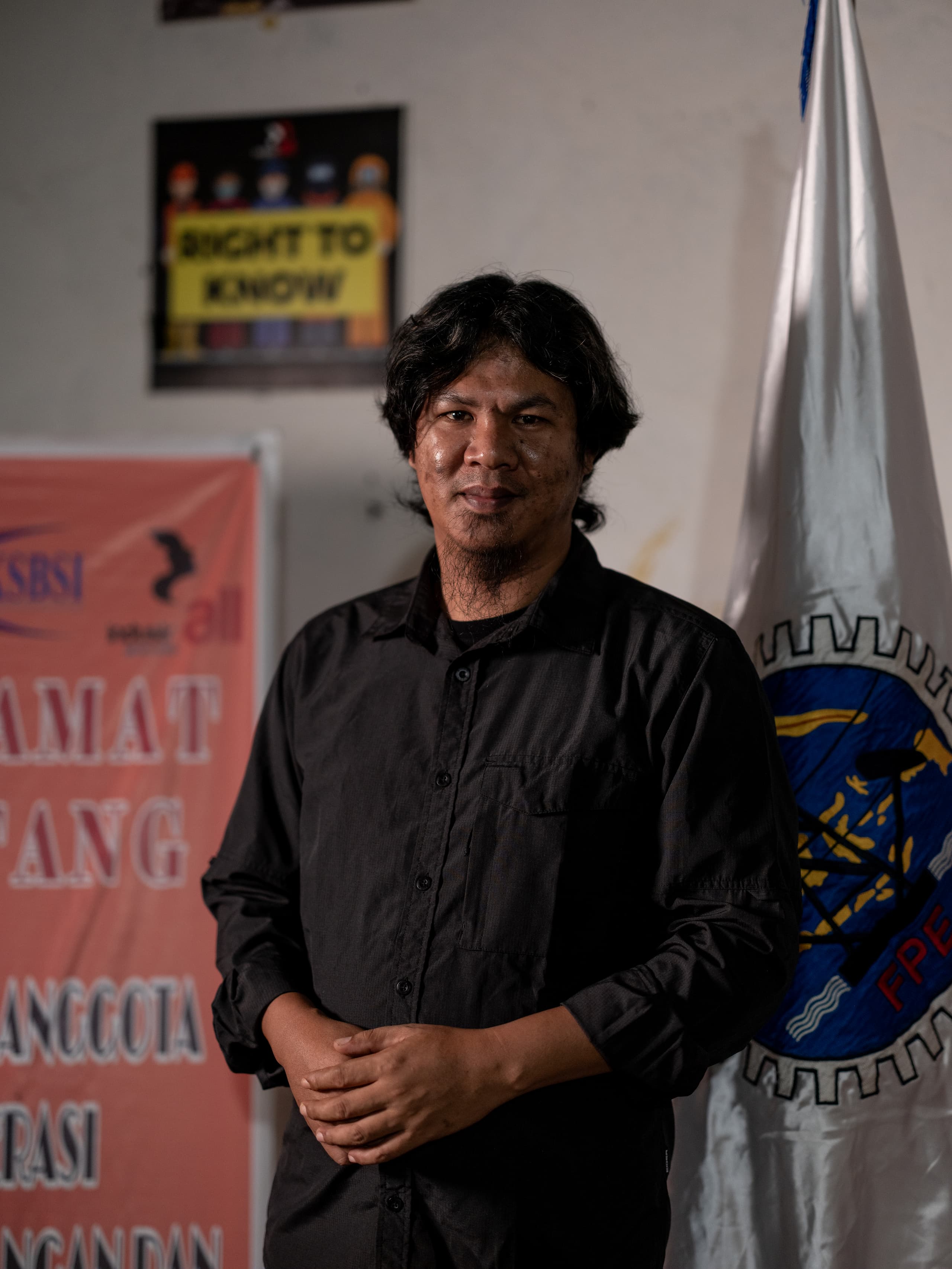 man in dark shirt standing next to a flag