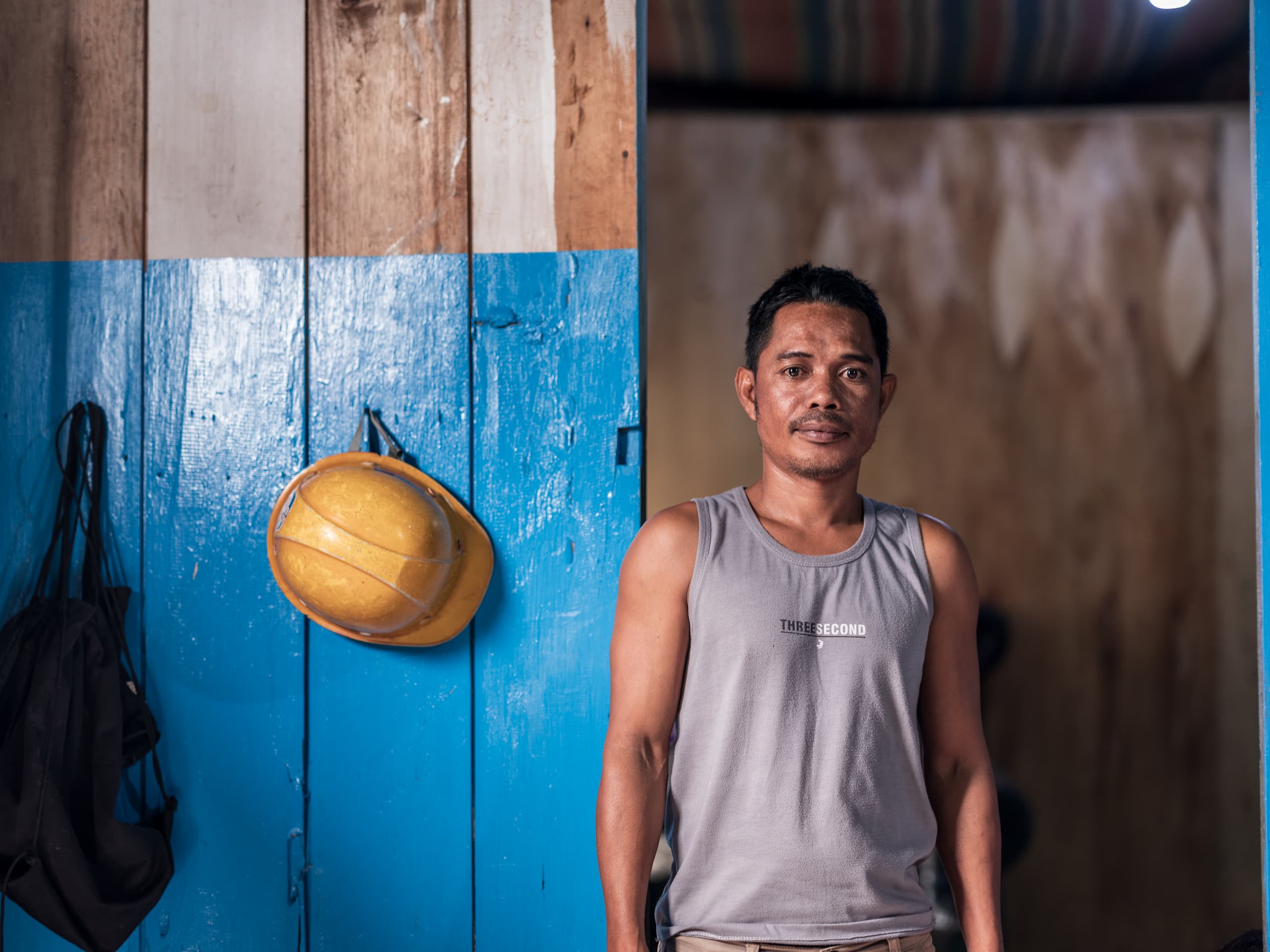man in sleeveless shit standing next to blue door.