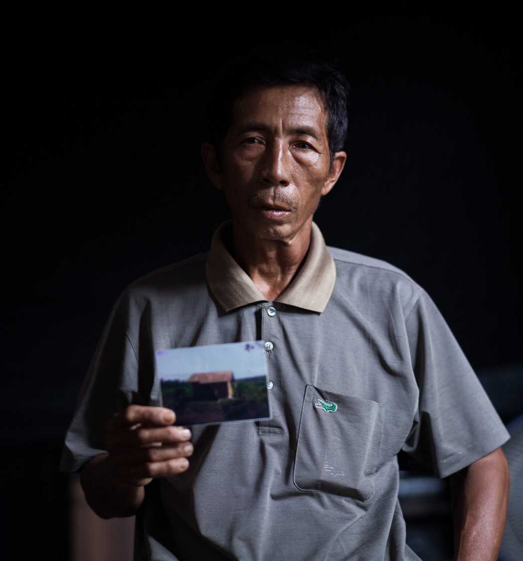 Marjuansyah, with a photograph of the hut destroyed when his land was taken by Triputra Agro Persada.